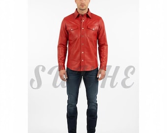 Op de afbeelding: Een persoon draagt een rood leren shirt met twee borstzakken en knoopsluitingen, gecombineerd met een donkerblauwe jeans en zwarte laarzen. Het shirt heeft een klassieke westernstijl.