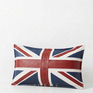 Pode incluir: Uma almofada retangular com a bandeira do Reino Unido, a Union Jack. O design apresenta um padrão de cruzes vermelhas, brancas e azul-marinho. A almofada é feita de couro ou material semelhante.