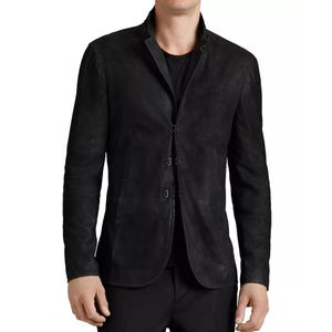 Può includere: Un blazer in pelle nera con collo a lupetto e chiusura a tre bottoni. La giacca ha maniche lunghe e una vestibilità su misura. La pelle sembra avere una finitura strutturata, che le conferisce un aspetto vissuto. Un capo di abbigliamento classico.