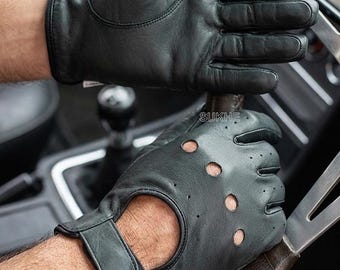 May include: A pair of black leather driving gloves featuring perforated knuckles, a cutout on the back of the hand, and a wrist strap with a hook-and-loop closure. The word SUKHE is printed in white on the back of the lower glove.