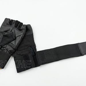 May include: A pair of black fingerless gloves featuring a textured palm area, a wide elastic wrist strap with a hook-and-loop closure, and a small tan leather tag attached to the cuff with the text SUKHE and ECHT LEDER printed on the surface.