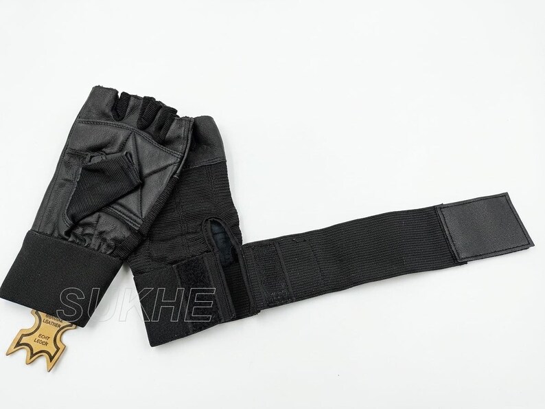 May include: A pair of black fingerless gloves featuring a textured palm area, a wide elastic wrist strap with a hook-and-loop closure, and a small tan leather tag attached to the cuff with the text SUKHE and ECHT LEDER printed on the surface.
