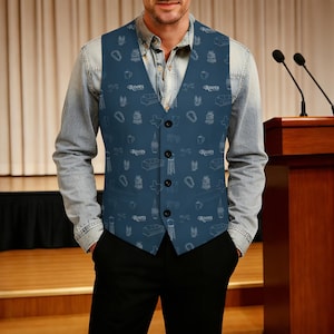 May include: A navy blue vest with a white pattern of various icons, including a sofa, a coffee mug, and the word "Roots". The vest is buttoned and worn over a denim shirt. The person is wearing black pants.