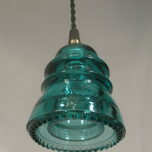 May include: A teal blue glass insulator pendant light fixture with a beaded edge and the text "MADE IN U.S.A." on the bottom.