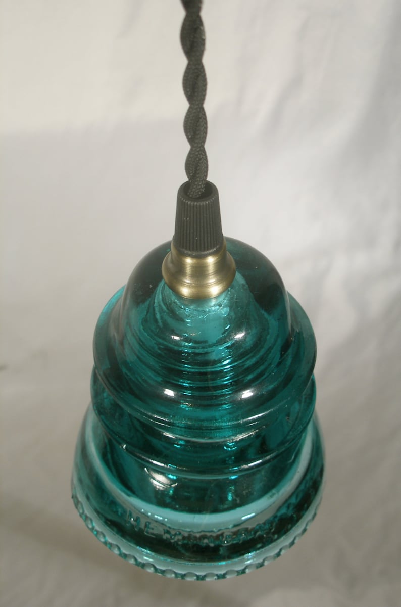 May include: A teal blue glass insulator pendant light with a black cord and brass socket.