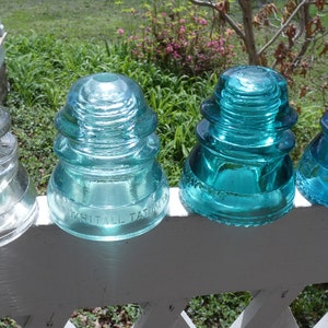 May include: Four glass insulators, one clear and three in shades of blue, with the text "Whitall Tatum" on one of the blue insulators.