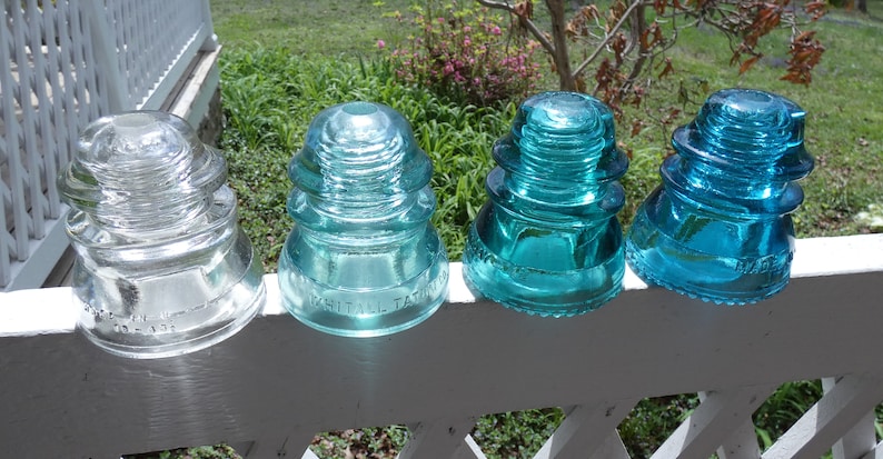 May include: Four glass insulators, one clear and three in shades of blue, with the text "Whitall Tatum" on one of the blue insulators.