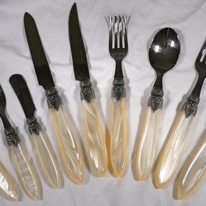 May include: A set of eight silver-plated flatware with ivory-colored handles. The set includes two forks, two spoons, two butter knives, and two dinner knives.