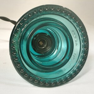 May include: A teal blue glass insulator with a beaded rim and the text "MADE IN USA" on the side.