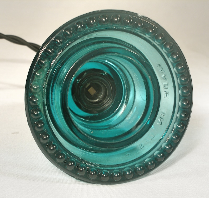 May include: A teal blue glass insulator with a beaded rim and the text "MADE IN USA" on the side.
