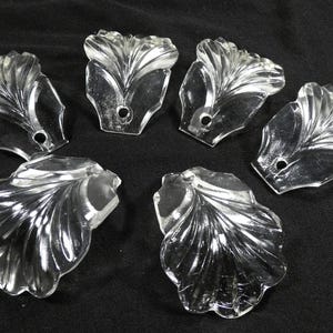 May include: Six clear glass crystal prisms with a leaf design. The prisms are faceted and have a hole at the top for hanging.