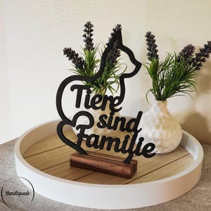 Könnte beinhalten: Schwarze Holz-Katzen-Silhouette mit dem deutschen Satz „Tiere sind Familie“. Das katzenförmige Schild steht auf einem Holzsockel, präsentiert auf einem weißen Tablett mit zwei weißen Vasen und Lavendel.