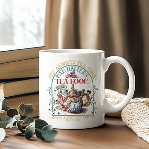 Puede incluir: Taza de cer&aacute;mica blanca con una ilustraci&oacute;n colorida de una tetera, un reloj y naipes. La taza tiene el texto "It's Always Tea Time, Mad Hatter's Tea Room, Serving Adventures and Tea Since 1965".