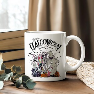 May include: White ceramic mug featuring a Halloween-themed design with characters and the text "This is Halloween." The mug has a curved handle and is decorated with bats, pumpkins, and various spooky figures.