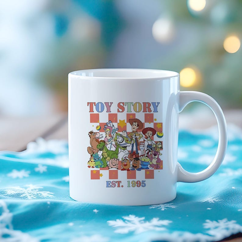 May include: White ceramic mug with a colorful illustration of the Toy Story characters, including Woody, Buzz Lightyear, and Jessie. The text "TOY STORY EST. 1995" is printed on the mug.