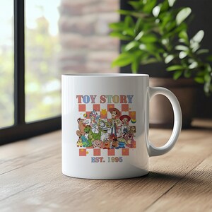May include: White ceramic mug with a colorful illustration of characters from the movie Toy Story. The mug has the text "TOY STORY EST. 1995" printed on it.