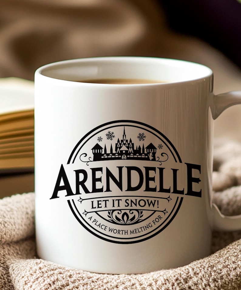 May include: White ceramic mug with a black circular design featuring the word "Arendelle" and the phrase "Let It Snow!" The design includes a castle silhouette and snowflakes. The mug is filled with a warm beverage.