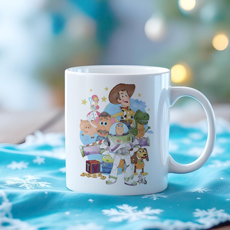 May include: White ceramic mug with a colourful illustration of characters from the animated film Toy Story. The design includes Woody, Buzz Lightyear, Rex, and other characters. The mug has a curved handle and is set against a blurred background.