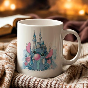 May include: White ceramic mug featuring a cartoon illustration of Stitch blowing a bubble in front of a castle. The design includes pink flowers and a blue watercolor background. The mug has a curved handle.