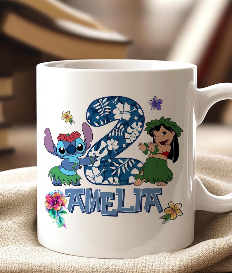 May include: White ceramic mug with a design featuring the number 2 in a blue floral pattern, Stitch and Lilo characters, and the name "AMELIA" in blue. The mug has a white handle and is decorated with colourful flowers.