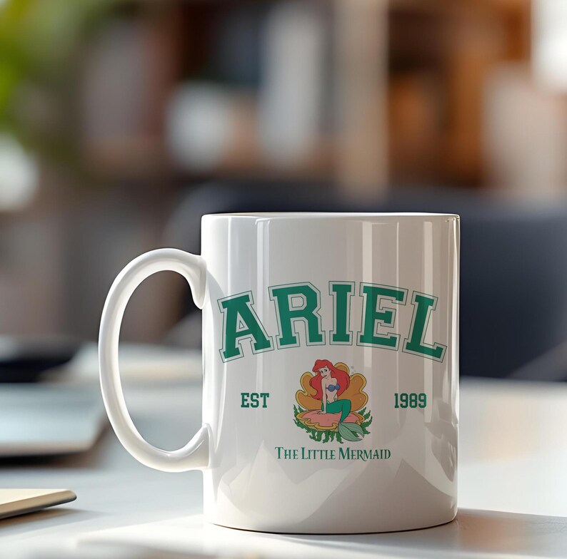 May include: White ceramic mug featuring the name "ARIEL" in green block letters, with "EST 1989" below. The Little Mermaid logo is in the center. A classic coffee mug for fans of the animated film.