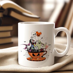 May include: White ceramic mug featuring a Halloween-themed design. The design includes characters from The Nightmare Before Christmas, inside an orange teacup with a jack-o'-lantern face. The mug is set on a tan cloth.