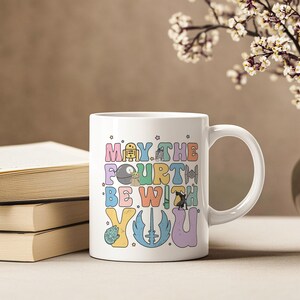 May include: White ceramic mug with a colorful graphic that says "May the Fourth Be With You" and features characters from Star Wars.