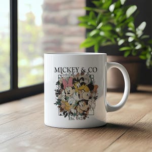 May include: White ceramic mug with a colorful illustration of Mickey Mouse, Minnie Mouse, Donald Duck, and Goofy surrounded by flowers. The text "Mickey & Co. Est. 1928" is printed on the mug.