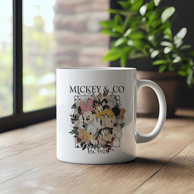 May include: White ceramic mug with a colorful illustration of Mickey Mouse, Minnie Mouse, Donald Duck, and Goofy surrounded by flowers. The text "Mickey & Co. Est. 1928" is printed on the mug.