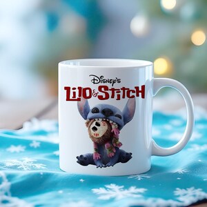 K&ouml;nnte beinhalten: Wei&szlig;e Keramik-Tasse mit Disney's Lilo & Stitch. Die Tasse zeigt Stitch, einen blauen Au&szlig;erirdischen, der ein braunes Objekt im Mund h&auml;lt. Die Tasse hat einen wei&szlig;en Henkel und das Disney's Lilo & Stitch-Logo in Rot.