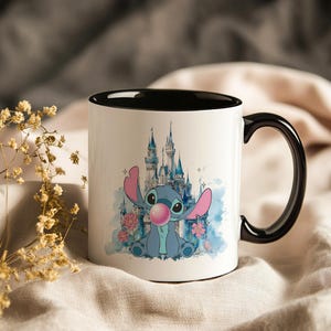 May include: White ceramic mug with a black interior and handle. The mug features a cartoon illustration of Stitch blowing a bubble, with a blue castle and pink flowers in the background. A fun and colorful design.
