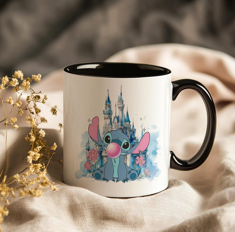 May include: White ceramic mug with a black interior and handle. The mug features a cartoon illustration of Stitch blowing a bubble, with a blue castle and pink flowers in the background. A fun and colorful design.