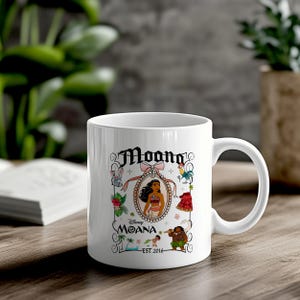 May include: White ceramic coffee mug featuring a colourful illustration of Moana from Disney's Moana. The illustration includes Moana, Maui, Pua the pig, Hei Hei the rooster, and a floral design. The text "Moana" and "Est. 2016" are printed on the mug.