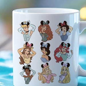 May include: White ceramic mug featuring illustrations of various cartoon princesses wearing mouse ear headbands. Each princess is depicted in a unique pose and outfit, with a colorful design. The mug has a white handle and a glossy finish.