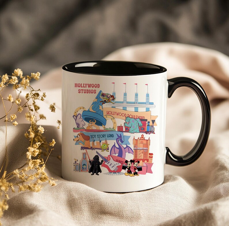 K&ouml;nnte beinhalten: Wei&szlig;er Keramikbecher mit schwarzem Henkel und Innenraum. Der Becher zeigt eine farbenfrohe Grafik von Hollywood Studios-Attraktionen und -Charakteren, darunter Mickey und Minnie Mouse. Der Text "Hollywood Studios" ist sichtbar.