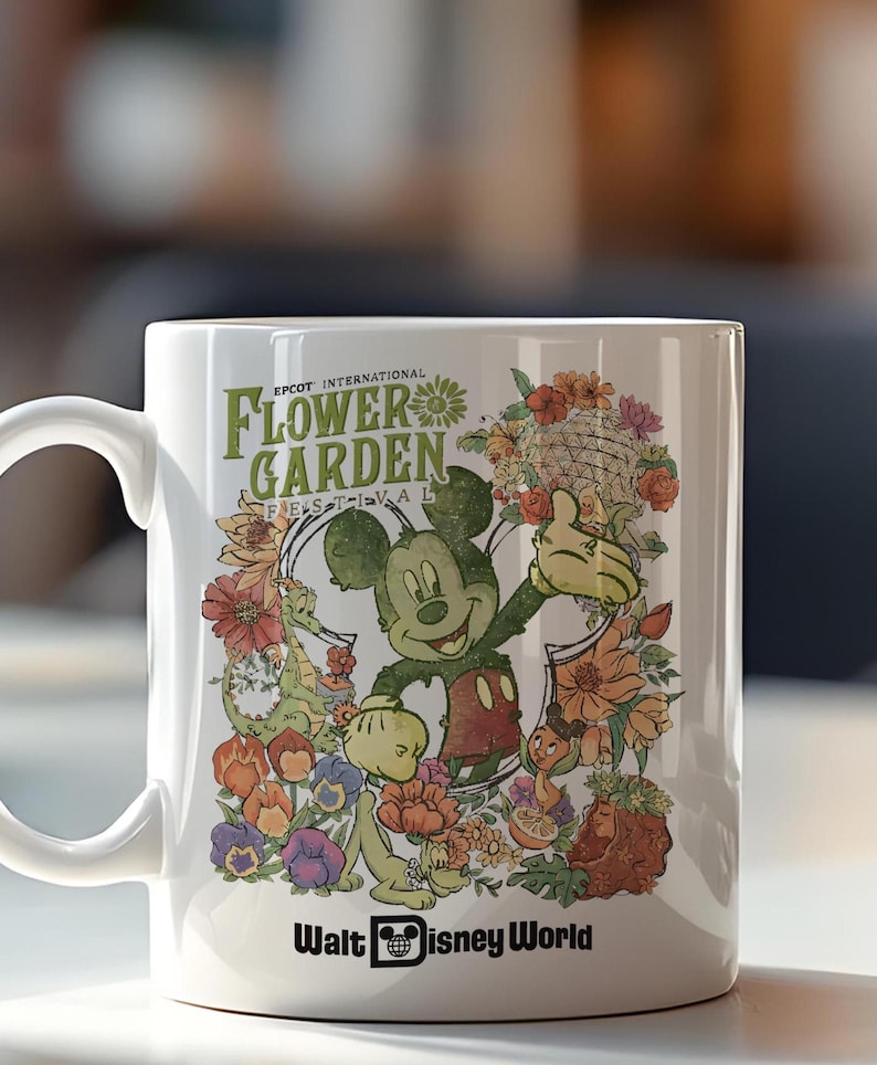 May include: White ceramic mug featuring Mickey Mouse surrounded by colourful flowers and the text "EPCOT INTERNATIONAL FLOWER GARDEN FESTIVAL" and "Walt Disney World". The design includes various floral elements and cartoon characters.
