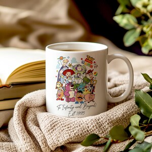 Pu&ograve; includere: Tazza in ceramica bianca con un'illustrazione colorata di personaggi del franchise Toy Story. La tazza ha il testo "Toy Story Land" e "To Infinity and Beyond! Est. 1995" stampato su di essa.