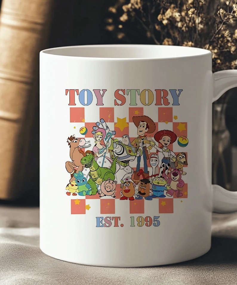 May include: White ceramic mug with a colorful graphic of the Toy Story characters, including Woody, Buzz Lightyear, Jessie, and Rex. The text "TOY STORY EST. 1995" is printed below the characters.