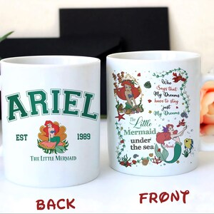 May include: White ceramic mug featuring the text "ARIEL" in green collegiate lettering, with an image of Ariel the mermaid. The mug also includes the text "EST 1989" and "The Little Mermaid". The other side has a design with Ariel and the text "Who Says that My Dreams have to stay just My Dreams".