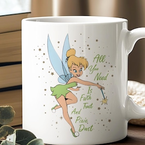 May include: White ceramic mug featuring a cartoon illustration of a fairy with blue wings and a green dress. The mug has the text "All You Need Is Faith Trust And Pixie Dust" in green. The mug has a curved handle.