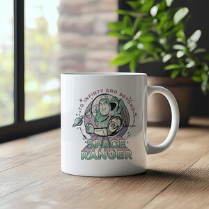 May include: White ceramic mug with a cartoon image of Buzz Lightyear from Toy Story. The design includes the words "To Infinity and Beyond" and "Space Ranger" in purple and green. The mug has a curved handle and is on a wooden surface.