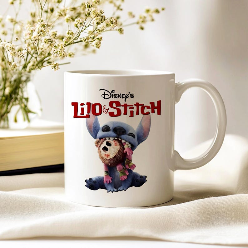 K&ouml;nnte beinhalten: Wei&szlig;e Keramik-Tasse mit Disney's Lilo & Stitch. Die Tasse zeigt Stitch, einen blauen Au&szlig;erirdischen, der einen braunen Teddyb&auml;ren im Mund h&auml;lt. Die Tasse hat einen wei&szlig;en Henkel und das Disney's Lilo & Stitch Logo in Rot.