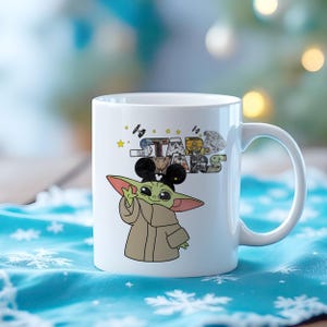 Może przedstawiać: Biały ceramiczny kubek z kresk&oacute;wkową ilustracją Grogu z Gwiezdnych Wojen, noszącego uszy Myszki Miki. Kubek ma logo Gwiezdnych Wojen z r&oacute;żnymi obrazami postaci. Uchwyt jest biały.