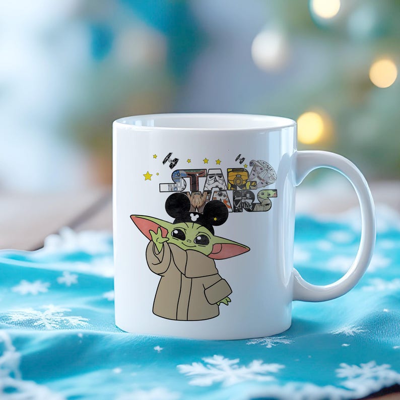 Może przedstawiać: Biały ceramiczny kubek z kresk&oacute;wkową ilustracją Grogu z Gwiezdnych Wojen, noszącego uszy Myszki Miki. Kubek ma logo Gwiezdnych Wojen z r&oacute;żnymi obrazami postaci. Uchwyt jest biały.