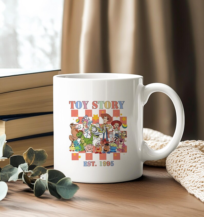 May include: White ceramic mug with a colorful illustration of characters from the Toy Story franchise. The mug has the text "TOY STORY" and "EST. 1995" printed on it.
