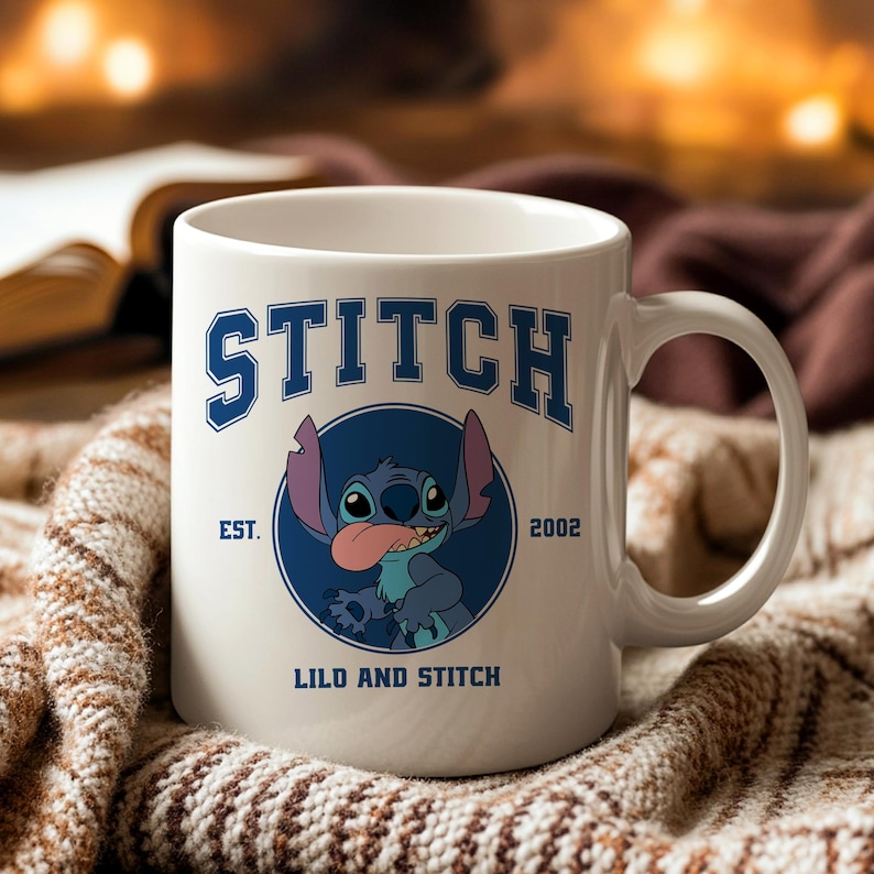 Puede incluir: Taza de cer&aacute;mica blanca con la palabra "STITCH" en letras azules y un gr&aacute;fico del personaje Stitch. La taza tiene el texto "EST. 2002" y "LILO AND STITCH". La taza tiene un asa curva y est&aacute; sobre un fondo c&aacute;lido y borroso.