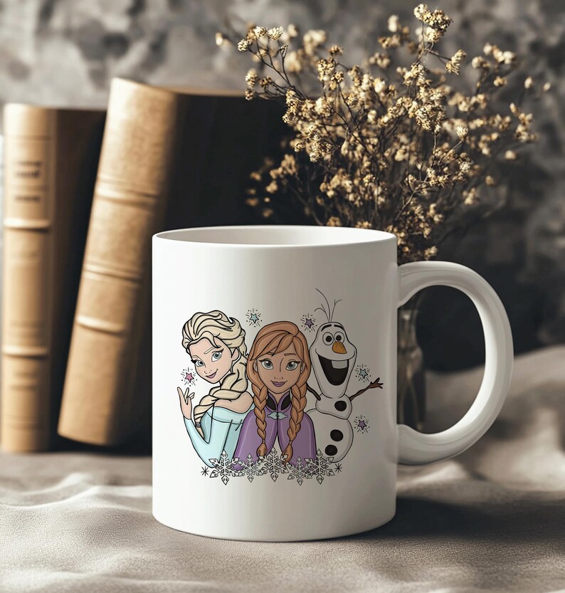 Puede incluir: Taza de cer&aacute;mica blanca con Elsa, Anna y Olaf de la pel&iacute;cula Frozen. Los personajes est&aacute;n representados en un estilo de dibujos animados colorido, con copos de nieve a su alrededor. La taza tiene un asa curva.