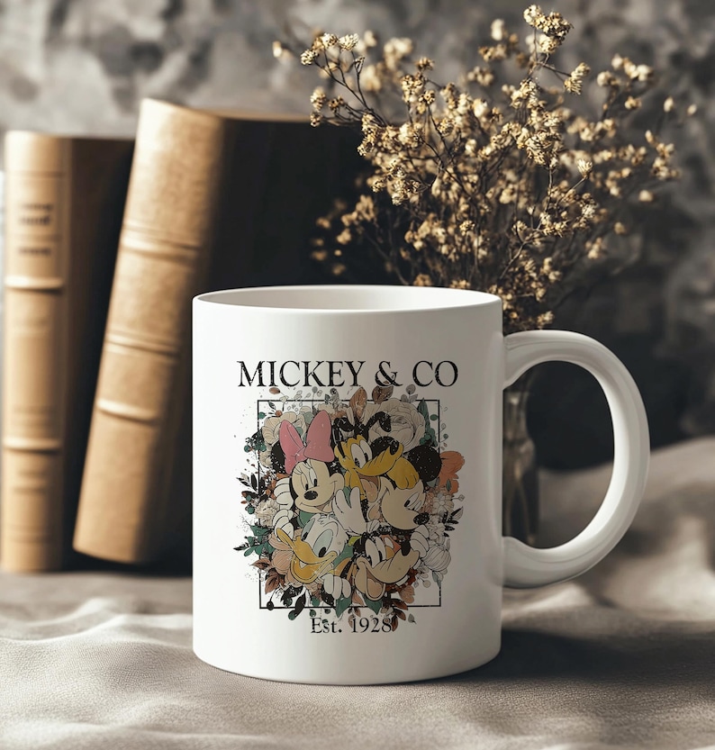 May include: White ceramic mug with a colorful illustration of Mickey Mouse, Minnie Mouse, Donald Duck, and Goofy surrounded by flowers. The text "MICKEY & CO. Est. 1928" is printed on the mug.