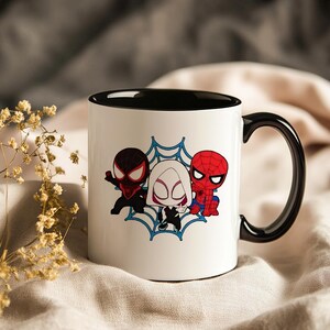 May include: White ceramic mug with a black interior and handle. The mug features a cartoon illustration of three Spider-Man characters in a blue web design. The characters are in red, black, and white.