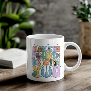 May include: White ceramic mug with a colorful design that says "May the Fourth Be With You". The design includes various Star Wars characters and symbols.